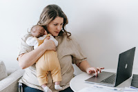 A new mom working on a laptop with her baby on her shoulder