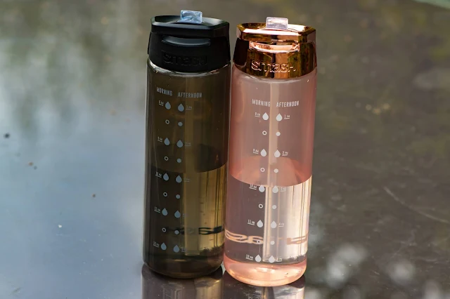 rose gold and black SMASH 700ml water bottles side by side on a glass table