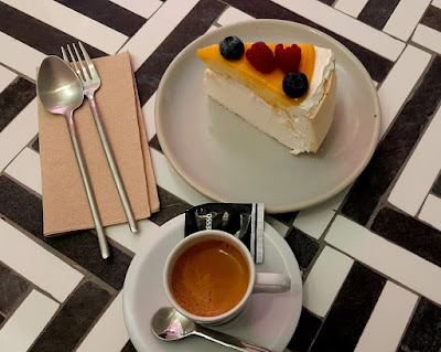 uma mesa preto e branco, uma xícara de café, e um prato com uma fatia de pavlova