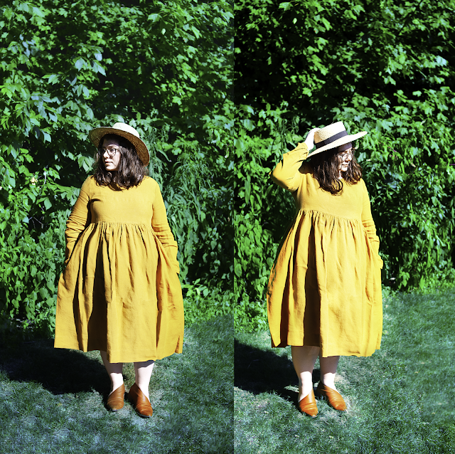 An outfit consisting of a straw boater hat, mustard yellow long sleeve linen smock dress, and cognac d'orsay flats.