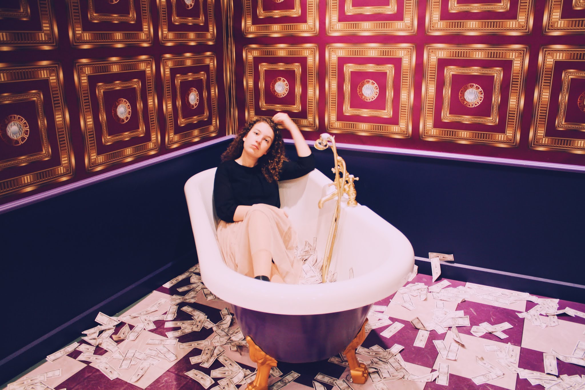 Ik zittend in een bad vol geld in een paars/gouden ruimte