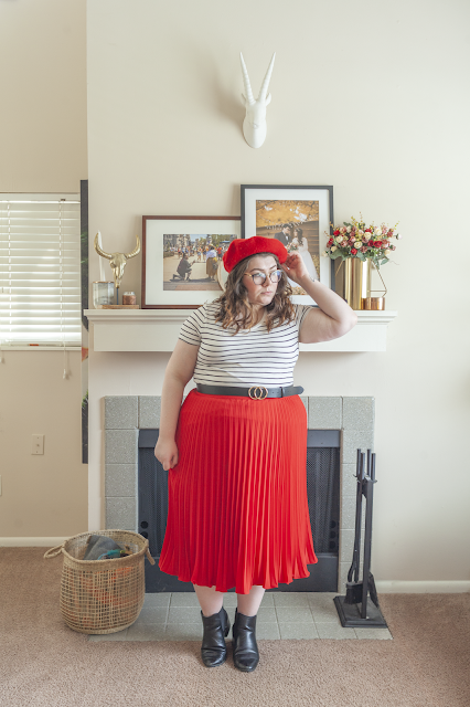 An outfit consisting of a red beret, white and black striped tee tucked into a red pleated midi skirt and black chelsea boots.