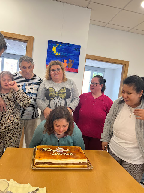 Chica rodeada de gente soplando las velas de una tarta de cumple