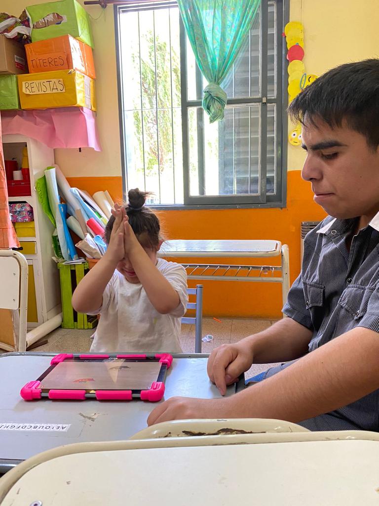 Gonzalo ayudando a utilizar una tablet a una estudiante de la escuela.