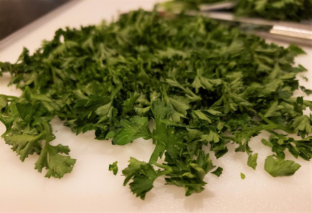 White cutting board with chopped parsley and knife in background