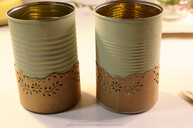 Two metal cans painted light green with brown decorative paper wrapped around bottom