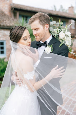 groom holding brides face with veil blowing in the wind