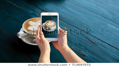 Mobile blog posts with smart phone over a white teacup cup of creamy beverage.