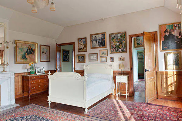 foto do quarto de Claude Monet com uma cama branca e muitos quadros nas paredes