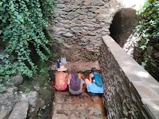 Three people from behind kneeling at the water source.