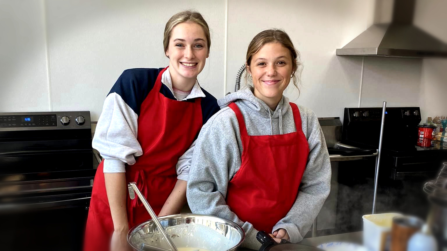 two young female cooks in kitchen with bowls of waffle batter