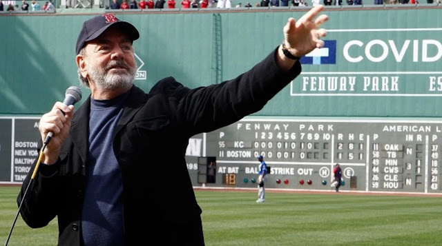 Neil Diamond stands with hiss back to the Fenway Park scoreboard and sings “Sweet Caroline” after the Boston Marathon Bombing.