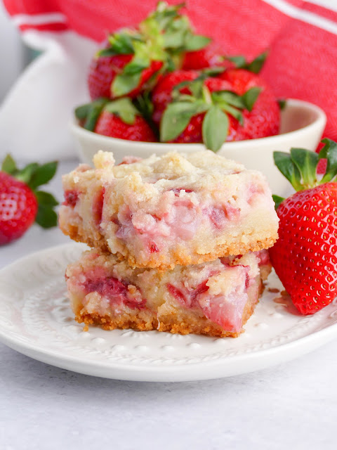 2 bars stacked on a white plate with fresh strawberries on the side.