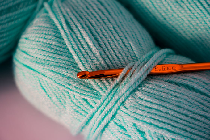 Novelo de lã ciano claro entrelaçado com uma agulha de crochê de 5,5 mm. A agulha é de metal e tem cor bronze