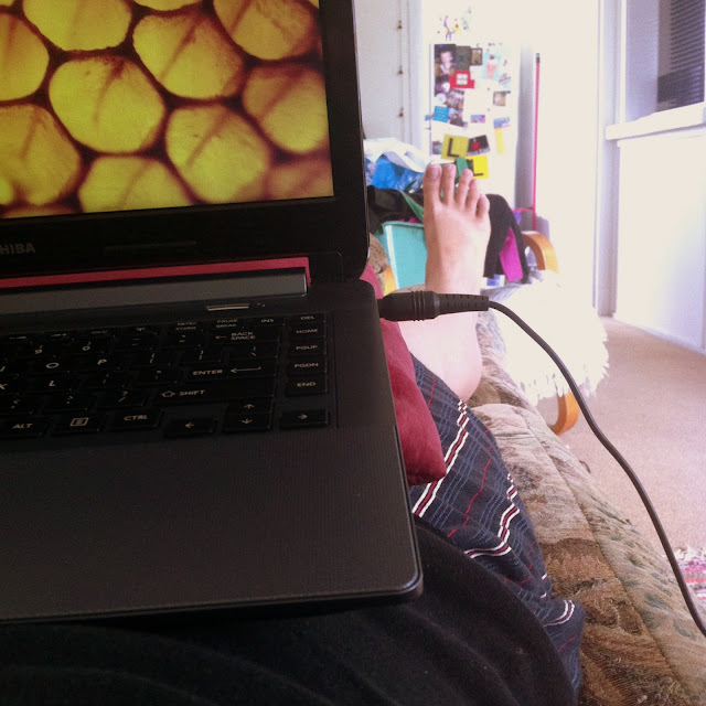 Photo of my view from the couch including my laptop on a cushion, my legs and the kitchen in the distance.