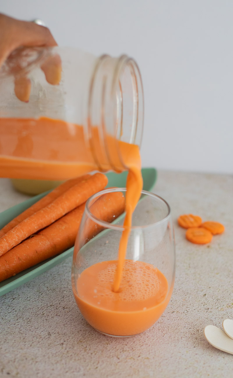 A picture of pouring carrot juice from a mason jar into a glass.
