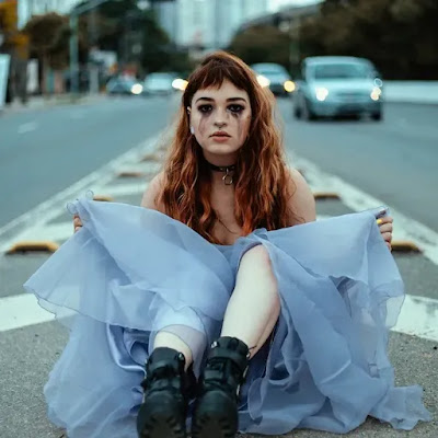 A girl with an ugly face and big frock sitting in between the road.