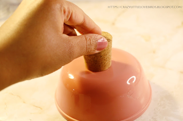 Hand holding cork on bottom of pink bowl