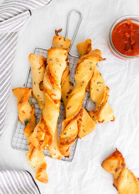 pizza twists on a parchment and wire rack background stacked in a pile.