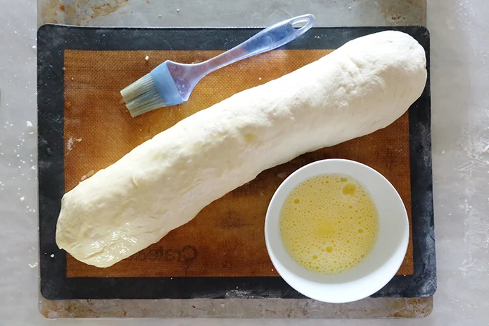 brushing egg wash onto rolled pepperoni bread on sheet pan