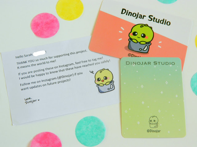 A photo showing a business card for Dinojar Studios, plus a thankyou note for backing their kickstarter project