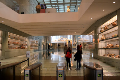 Image of the New Acropolis Museum entrance, with pottery left and right, the Archaic room ahead and the Caryatids above and a very prominent no photography sign