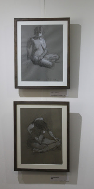 Two drawings of seated nude women on gallery wall