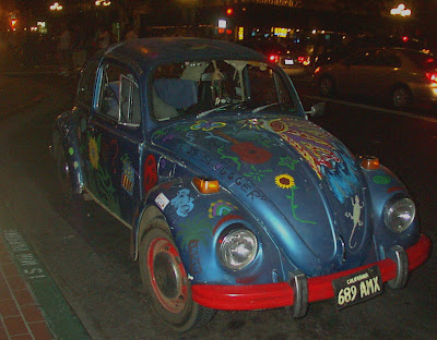 This is a side view of a classic Volkswagen Beetle.  Painted on the Beetle is a sunflower, America flag, and large butterfly