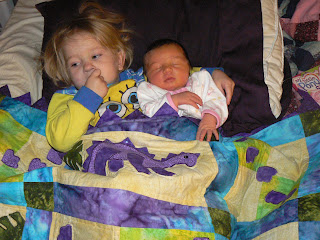 LIly premature preemie baby holds her newborn sister Nadia under a homemade dinosaur quilt 