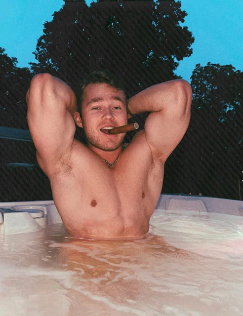Super muscular cute dude smiling with a cigar in his mouth sitting in the hot tub