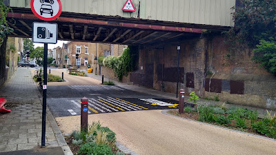 The street closer to the railway bridge with a pair of no motor traffic signs and the planting on both sides.