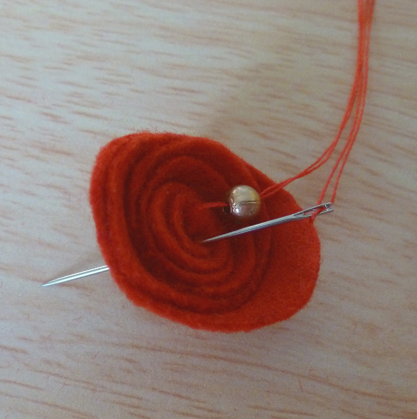 Sewing gold color bead into middle of a red felt flower