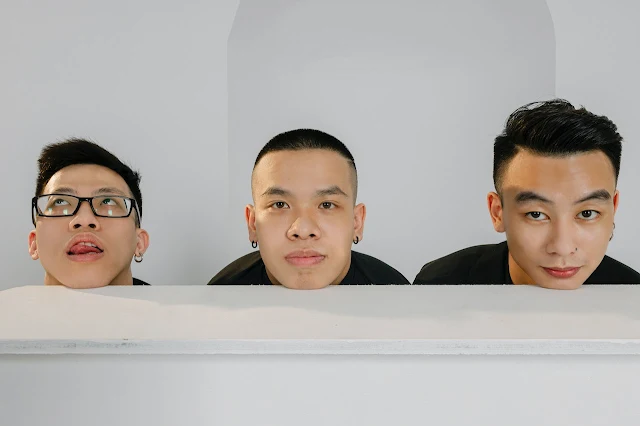 Three Asian boys with unique expressions, one wearing glasses, one with a serious demeanor, and one with well-groomed eyebrows and earrings.