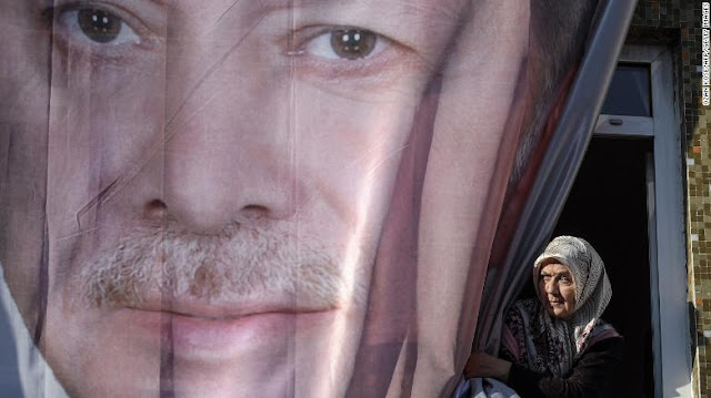 A woman peers out from behind a giant poster of Erdoğan during a March rally in Kasımpaşa