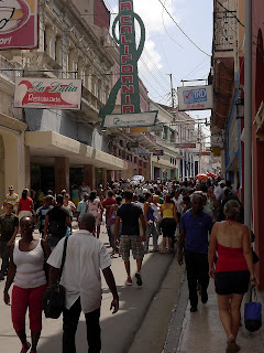 Santiago de Cuba, Fußgängerzone in der Altstadt. In der engen Straße drängen sich die Menschen, darüber viele Reklameschilder.