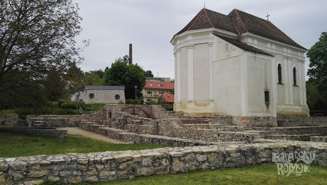 Előtérben középkori falmaradványok. Kicsit hátrébb jobbra ajezsuita templom álló, fehér falai.