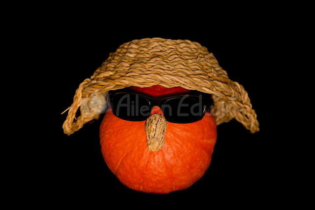 An orange pumpkin wearing sunglasses and hat on a black background