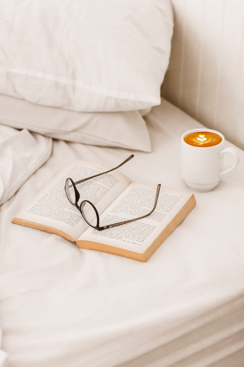 an opened book with eye glasses on top of a bed