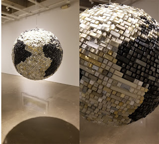 A large 3D globe suspended in air, the surface is covered in computer keyboard keys. Titled "There are Places on the Map that Don’t Exist” by Bart Vargas, keyboard keys, plastic bottles, foam, cardboard, paint, adhesive, hardware.