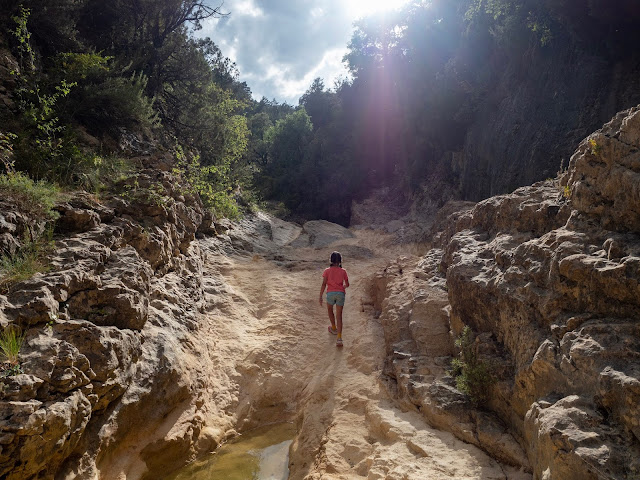 Niña de espaldas co el sol detrás caminando por el lecho del río en las pozas de San Martín (Huesca)