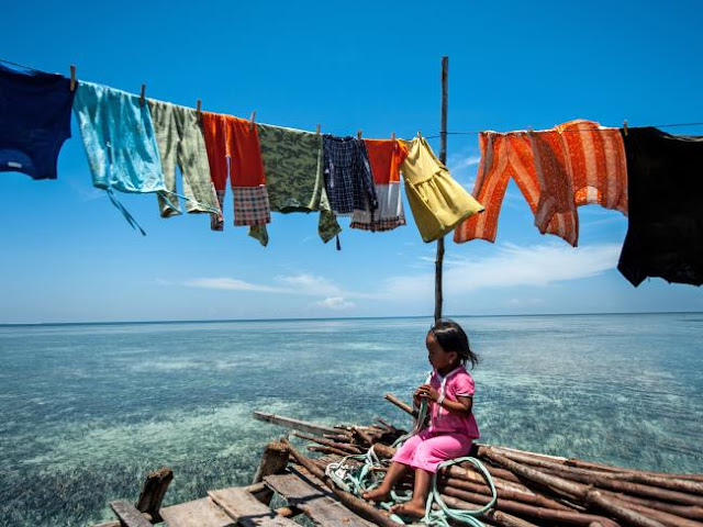 Ng Choo Kia - Menina sentada em pilhas de madeira em sua casa sobra a agua, os Bajau praticamente não tem acesso a terra firme, podendo contar apenas com algumas micro ilhas ao longo de seu território