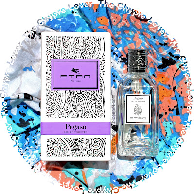 The bottle and paisley-laden box (black lines on a white background) lying flat on a grafitti-looking blouse (blue, peach, orange, blue, white, black)