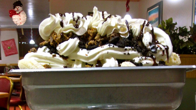 a metal kitchen sink piled high with bananas, soft serve ice cream, and toppings