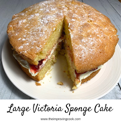 Large Victoria Sponge cake on a white plate, with one slice cut out.