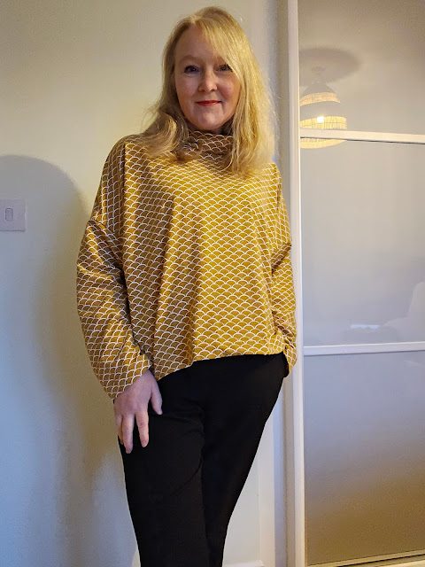 middle aged blonde white woman wearing mustard gold home sewn top with black trousers
