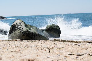 A rock in the middle of the beach with the sea splashing from behing