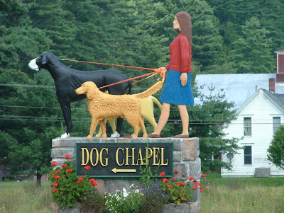 Statue of a Woman walking Three Dogs with sign that points to the Dog Chapel