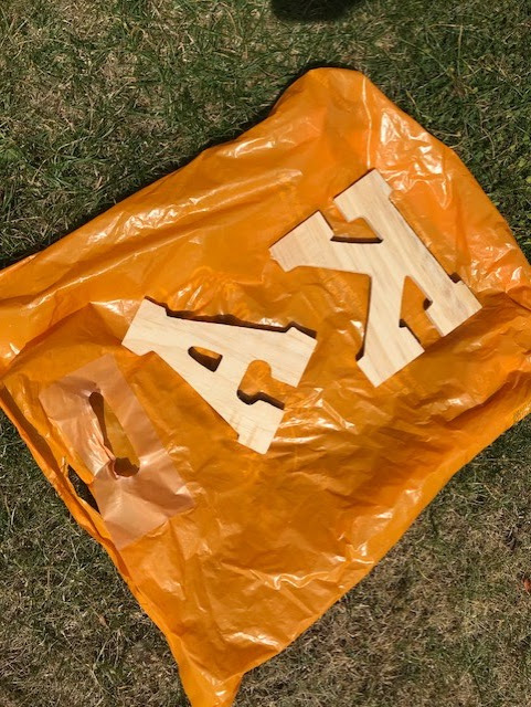 Plastic bag laid out on grass with the wooden letters laid on their front