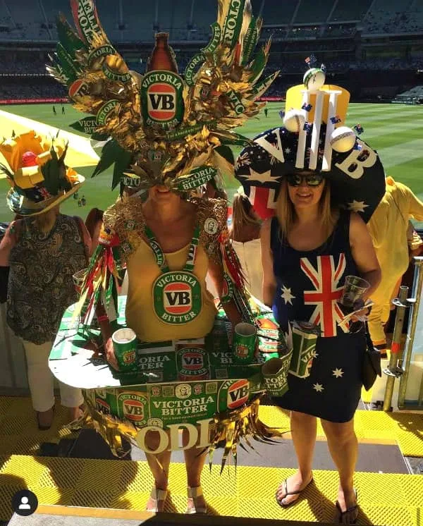 two women standing at cricket match dressed in elaborate paper costumes resembling a drinks bar