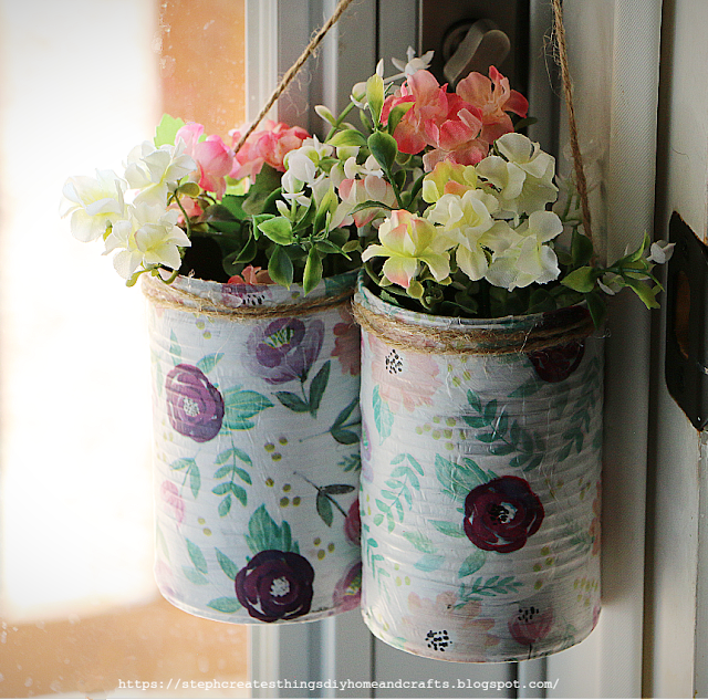 Decoupaged cans with floral print hanging with faux floral displayed inside of each can
